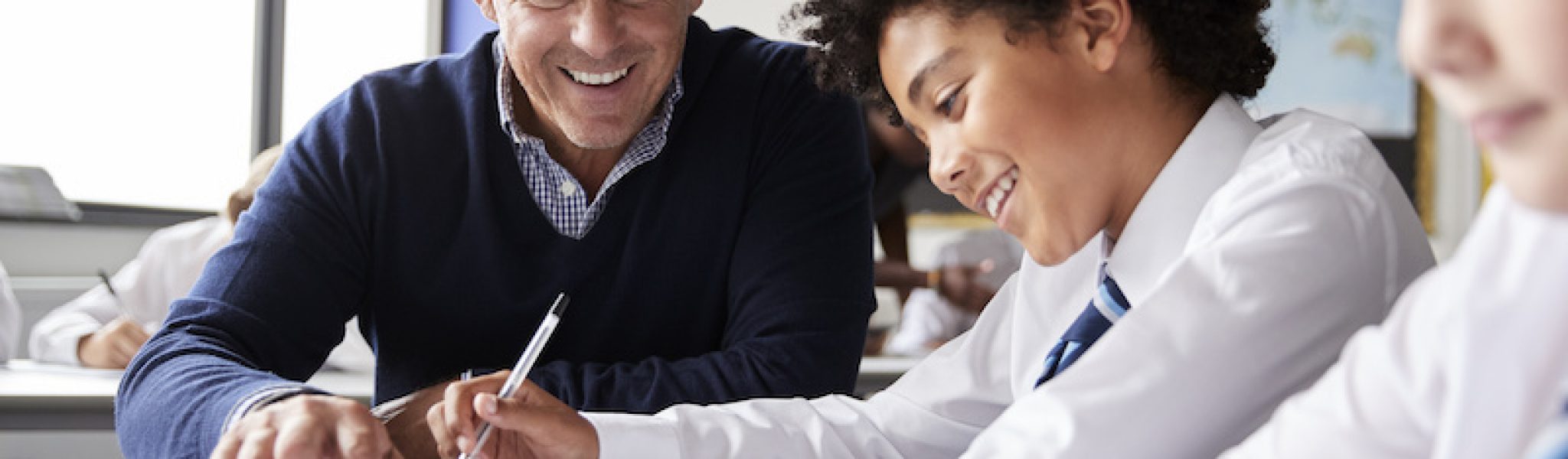 High School Tutor Giving Male Student Wearing Uniform One To One Tuition At Desk