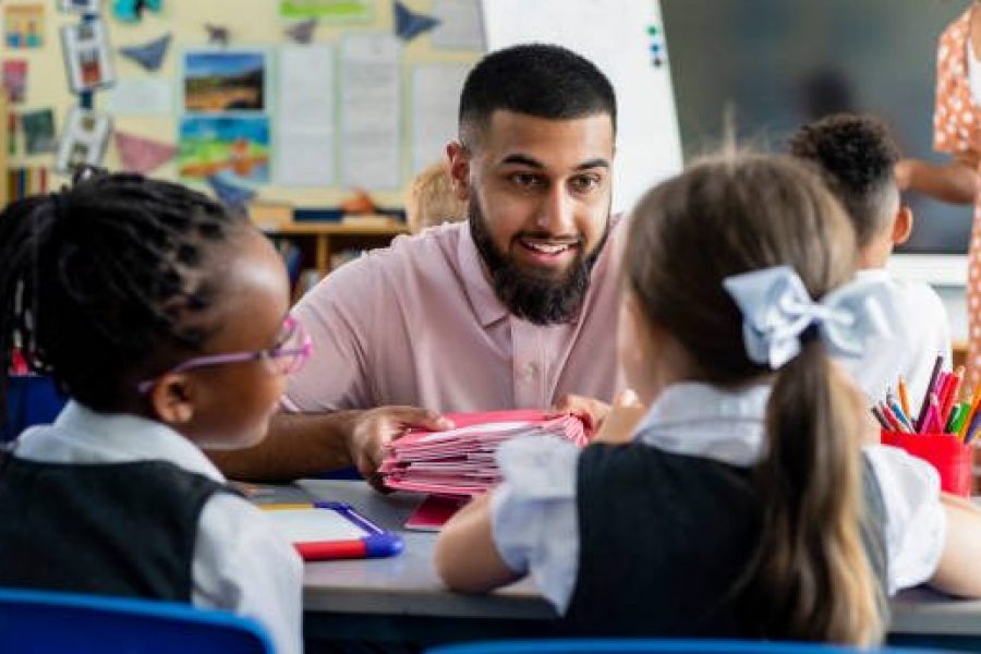 Primary school students sitting in a classroom being taught by a teacher who is crouched in front of them in the North East of England.