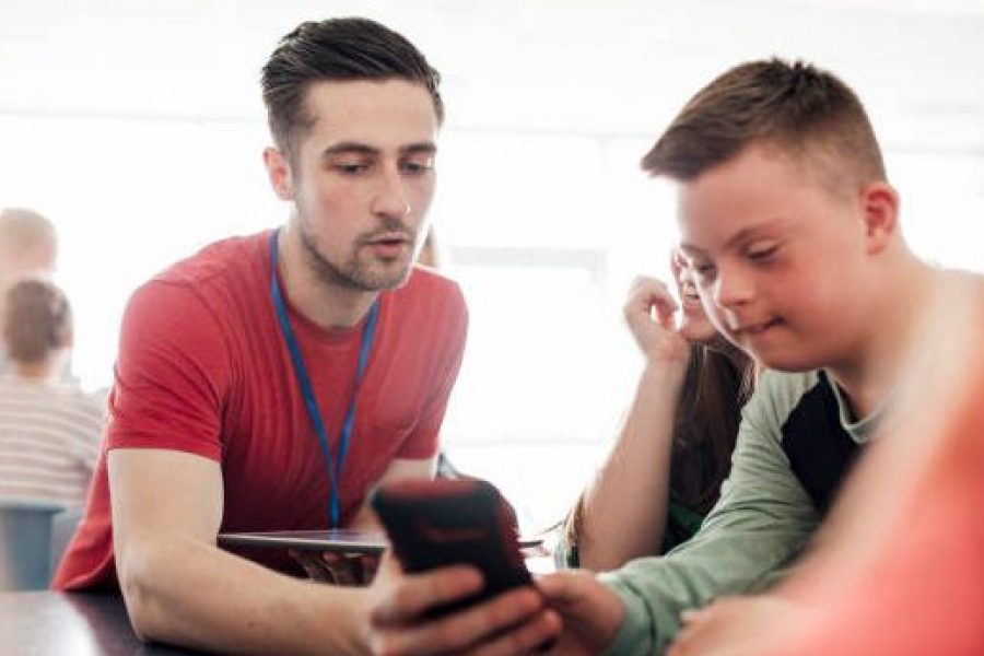 Point of view angle of teacher assisting down syndrome boy with using the smart phone.